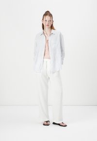Striped blue and white button-up shirt over a pink top, paired with white wide-leg pants and black flip-flops, minimalistic design.