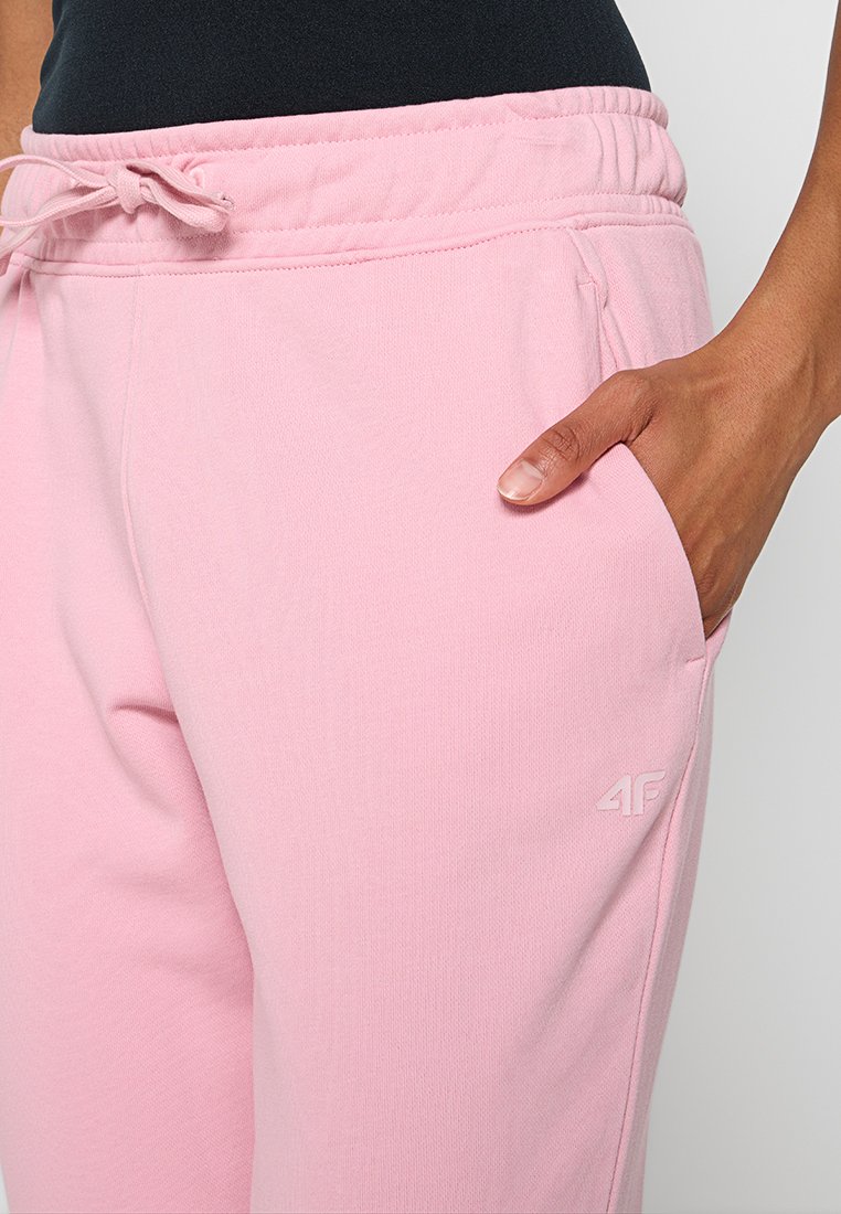 Zbliżenie na osobę ubraną w różowe dresowe spodnie z elastycznym pasem i sznurkiem, ręka spoczywająca w prawej kieszeni.
