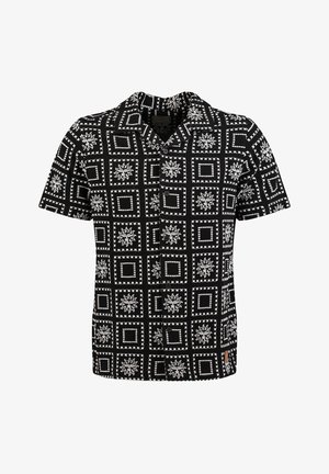 Chemise noire à manches courtes avec boutons, présentant des motifs de carrés blancs et de soleils disposés en grille sur le tissu.