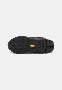 Black hiking shoe sole with deep treads for traction. Features a yellow rubber accent and rugged texture for durability.