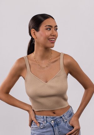 Beige geribbelde crop top met een V-halsontwerp en dikke banden, gecombineerd met hoog-wijde lichtblauwe denim shorts. Gouden kettingaccent.