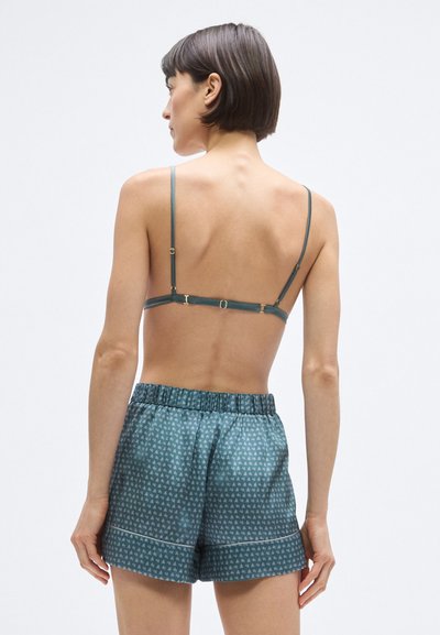 Bralette di raso turchese con spalline regolabili e dettagli in oro, abbinato a pantaloncini coordinati stampati con vita elasticizzata e orlo.