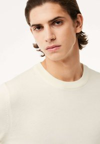 Cremfarbener Pullover mit geripptem Rundhalsausschnitt und strukturiertem Strick. Nahaufnahme des Oberkörpers eines Models, das den glatten Stoff und die Passform zeigt.