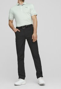 Polo gris clair avec une finition texturée et un logo, associé à un pantalon noir et des baskets blanches. Ceinturé, avec une coupe ajustée.