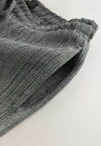 Grauer strukturierter Stoff mit vertikalen Streifen, ausgestattet mit einem elastischen Bund und einer lockeren Passform. Nahaufnahme der Oberfläche des Stoffes.