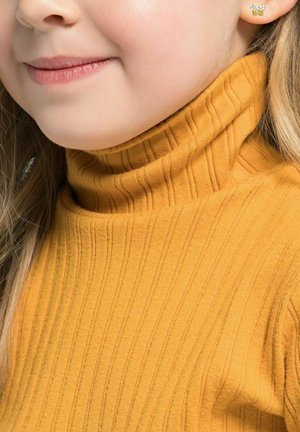 Maglione a collo alto giallo a coste con una vestibilità aderente, caratterizzato da un motivo testurizzato. Capelli biondi corti parzialmente visibili, con un piccolo orecchino a forma di farfalla.