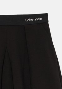 Čierne nohavice Calvin Klein s elastickým pásom so bielym logom, obsahujúce predné záhyby a bočné vrecká.