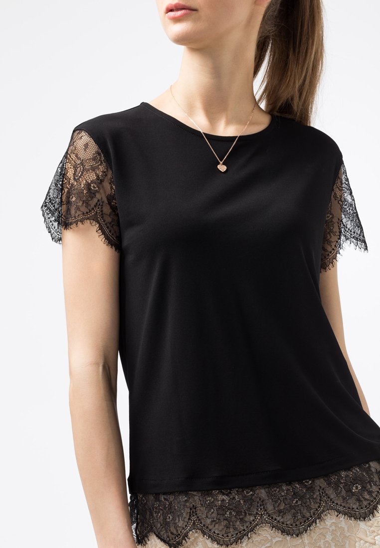 Top nero a maniche corte con rifiniture in pizzo sulle maniche e sull'orlo. Tessuto morbido, scollatura tonda, abbinato a una collana delicata.
