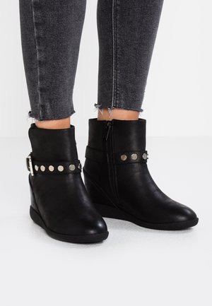 Zwarte sleehak enkellaarsjes met rits aan de zijkant en decoratieve zilverkleurige studs, gedragen met zwart skinny jeans met rafelige zoom.