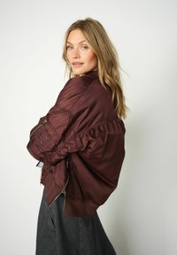 Bordoo bomber jakk, millel on sile ja läikiv viimistlus, puffitud varrukad, lukuga taskud ja soonikkudum. Kandsid tumeda teksaseeliku peal.