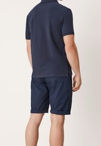 Granatowa koszulka polo z krótkim rękawem w połączeniu z granatowymi szortami. Szorty mają podwinięte mankiety i luźny krój, wykonane z lekkiego materiału.