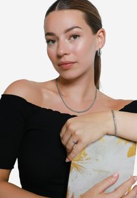 Collier et bracelet en argent tressé, boucles d'oreilles en forme d'anneau mat, modèle portant un top noir décolleté, tenant un carnet à motifs jaune et blanc.