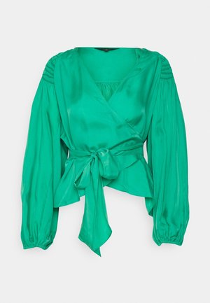 Blouse portefeuille en satin vert avec manches longues bouffantes, détails texturés aux épaules et taille nouée. Surface lisse avec une finition brillante.