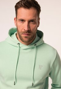 Felpa verde menta realizzata in tessuto morbido, con una tasca a marsupio frontale, coulisse e un logo sottile sul petto. Design semplice.