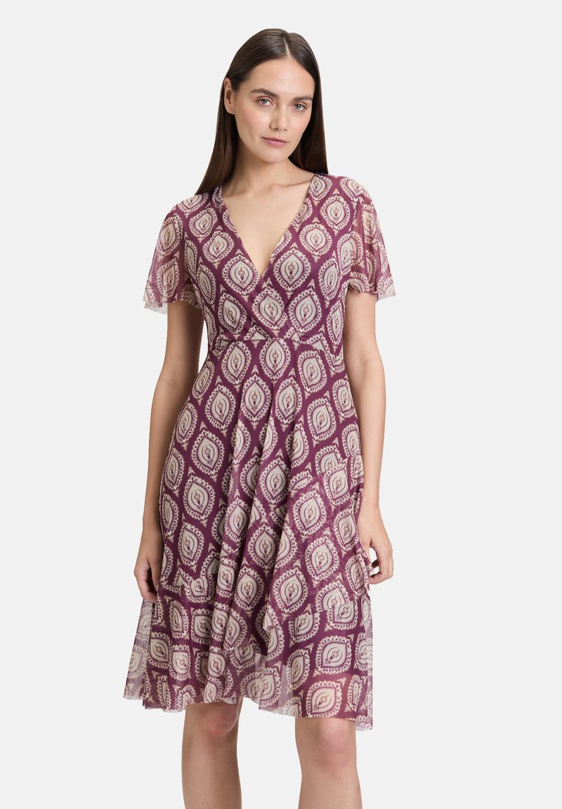 Lila Kleid mit kurzen, flatternden Ärmeln, einem V-Ausschnitt und einem fließenden Rock. Verfügt über ein cremefarbenes Paisleymuster überall. Leichter Stoff.