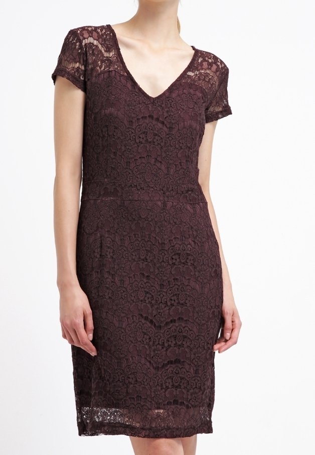 Femme portant une robe en dentelle violet foncé, à manches courtes et longueur genou, avec un décolleté en V sur fond blanc.