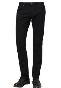 Černé slim-fit džíny s předními kapsami a zapínáním na knoflík, nošené s černými koženými šněrovacími botami na bílém pozadí.