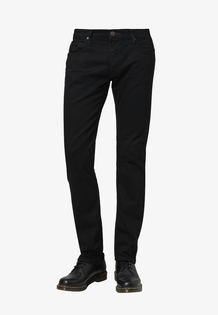 Černé slim-fit džíny s předními kapsami a zapínáním na knoflík, nošené s černými koženými šněrovacími botami na bílém pozadí.