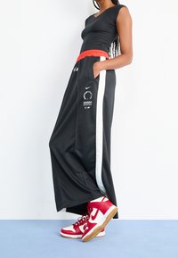 Svarta träningsoverallbyxor med röd elastisk midja, vita sidostripes och logodetalj. Tillsammans med röd och vit högskomodell.