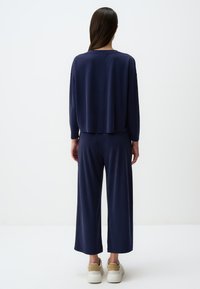 Navy Freizeitanzug bestehend aus einem lässigen Oberteil mit langen Ärmeln und weiten Hosen, gefertigt aus weichem Stoff, kombiniert mit weißen Sneakers.