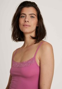 Pink sleeveless top with lace trim along the neckline, made from a soft fabric. Simple design and fitted shape, highlighting the texture.