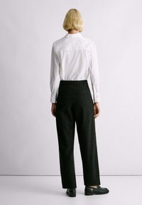 Camicia bianca con colletto, maniche lunghe e yoke posteriore, abbinata a pantaloni neri a vita alta con una sottile trama a pois.
