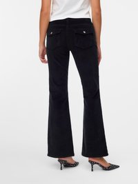 Des pantalons évasés en velours côtelé noir avec une taille mi-haute, des poches arrière avec des boutons en métal et une texture lisse. Associés à des talons noirs à pois.