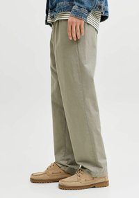 Pantalon large vert olive clair à texture lisse avec des plis à l'avant, associé à des chaussures à lacets couleur tan.