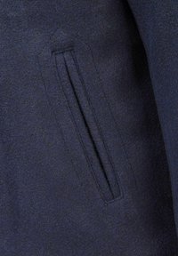 Tumedat sinise villase kangas, millel on sile tekstuur. Külje peal on peidetud lukuga tasku ja struktureeritud õmblusdetailid.