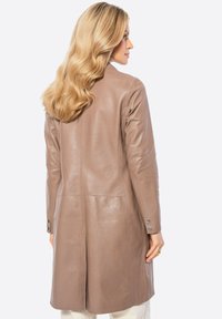 Bruine leren jas met een getailleerde pasvorm, lange mouwen en een gladde textuur. Beschikt over platte naden en knoopaccenten op de manchetten.