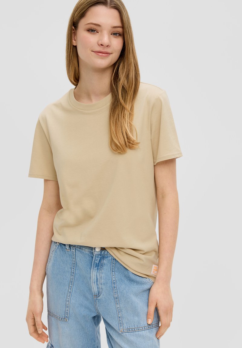 Beige katoen t-shirt met een ronde hals en korte mouwen, gecombineerd met lichtblauwe denim broek. Voorzien van een klein oranje label aan de zoom.