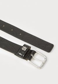 Ceinture en cuir noir présentant un design texturé, une boucle en métal argenté et un détail de logo près de la boucle. Plusieurs trous pour un ajustement réglable.
