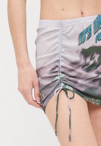 Minifalda fruncida con un patrón de tie-dye, que cuenta con una cinturilla elástica y cordones a los lados. El material parece suave y ligero.