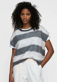 Maglione lavorato a maglia in morbidi toni di grigio e bianco a righe, con collo rotondo, maniche corte e vestibilità rilassata, indossato su pantaloni grigio chiaro.