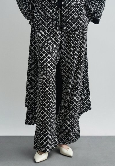 Tenue à motifs noir et blanc avec un pantalon ample et une veste courte assortie, présentant un design géométrique et un tissu doux. Souliers blancs délicats.