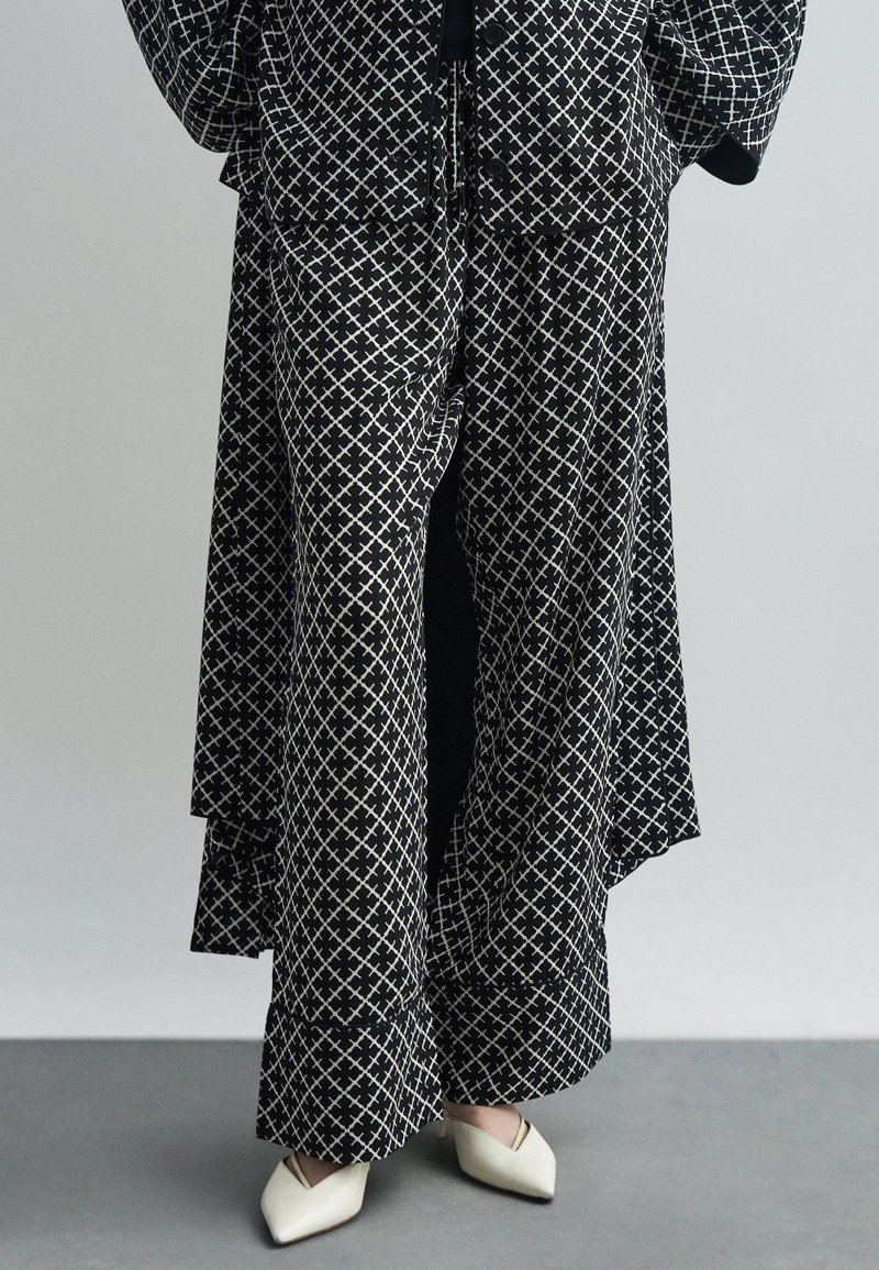 Μαύρο και λευκό σχέδιο ρούχων με φαρδιά παντελόνια και ταιριαστό κοντό σακάκι, με γεωμετρικό σχέδιο και μαλακό ύφασμα. Λεπτές άσπρες παπούτσια.