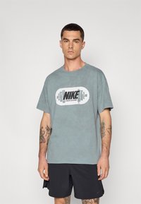 Grå bomulds t-shirt med et stort sort og hvidt Nike-logo centreret. Korte ærmer og afslappet pasform. Båret med sorte træningsshorts.