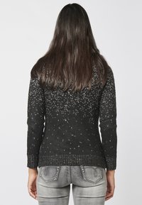 Knitted black sweater featuring a textured pattern with silver accents, long sleeves, and a ribbed hem, paired with grey jeans.
