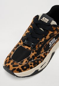 Sneaker med leopardmønster som har svarte netting- og tekstil detaljer, med svarte snørebånd og tunge. Gummisåle med en beige mellomsåle, merket detalj.
