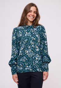 Grünes Oberhemd mit Blumenmuster in Blau, Creme und zartem Gelb. L�ängerer Puffärmel und Kragen, aus leichtem Stoff gefertigt.