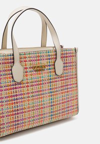 Kolorowa torebka na ramię z plecionej tkaniny z kremowymi skórzanymi uchwytami i złotym logo GUESS z przodu, na białym tle.