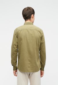 Olive zöld, hosszú ujjú ing, egyenes aljjal, gombbal zárható mandzsettákkal és gallérral. Az anyag puhanak és tartósnak tűnik. Egyszerű dizájn, minta nélkül.