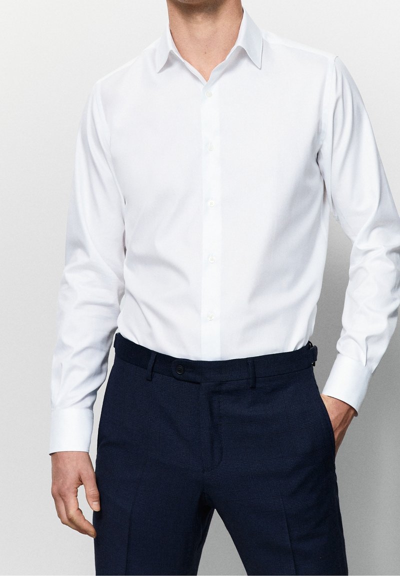 Witte blouse met lange mouwen en een klassieke kraag, gecombineerd met donkerblauwe, gemusterde broek met een soepele textuur en een slim fit ontwerp.