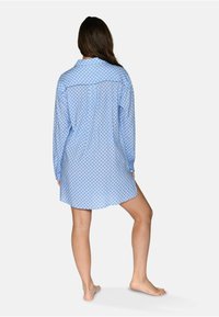 Abito camicia a maniche lunghe di colore azzurro chiaro con un motivo a rombi, orlo arrotondato e colletto. Il tessuto sembra liscio e leggero.