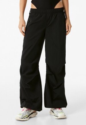 Zwarte wijde broek van lichtgewicht stof, met een elastische tailleband en zijzakken, gecombineerd met stevige, meerkleurige sneakers.