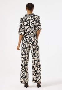 Bloemmotief outfit met een zwart en crème kleurenschema; gemaakt van lichtgewicht stof, met brede broekspijpen en korte, puffed mouwen.