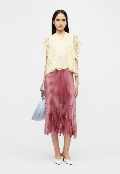 Κίτρινο τοπ με δαντέλα επάνω και μανίκια με βολάν· ροζ πλισέ φούστα με κεντήματα λουλουδιών· αξεσουάρ με τσάντα σε ανοιχτό μπλε και λευκές γόβες.