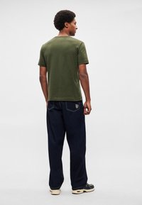 Λαδί βαμβακερό T-shirt με κοντά μανίκια, συνδυασμένο με άνετο σκούρο μπλε τζιν παντελόνι με ραφή λεπτομέρεια στην πίσω τσέπη.