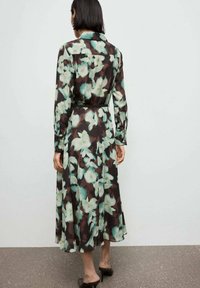 Abito lungo e trasparente di colore marrone scuro con grandi motivi floreali verde chiaro. Presenta un colletto, maniche lunghe e una cintura nera in vita.