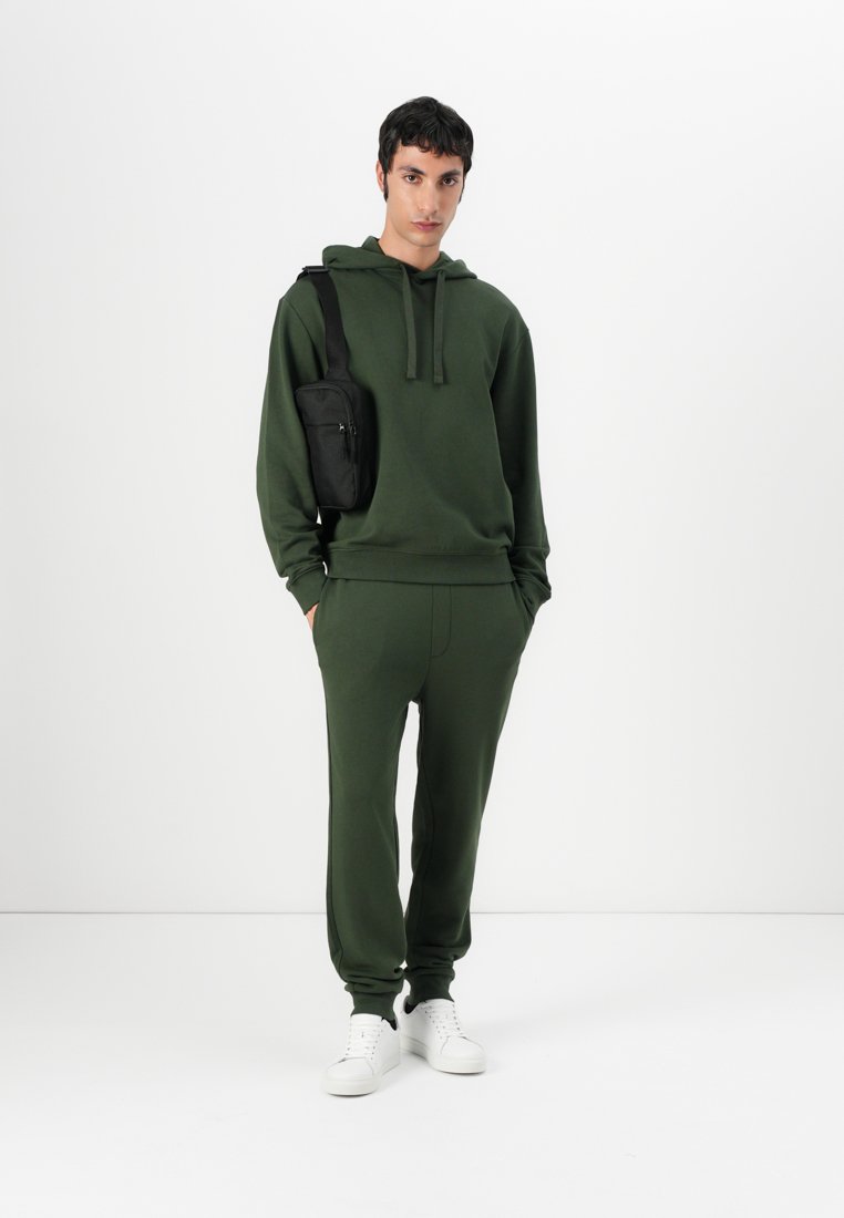 Sweatshirt vert et jogging assorti en tissu doux, avec une coupe décontractée. Associé à un sac bandoulière noir et des baskets blanches.